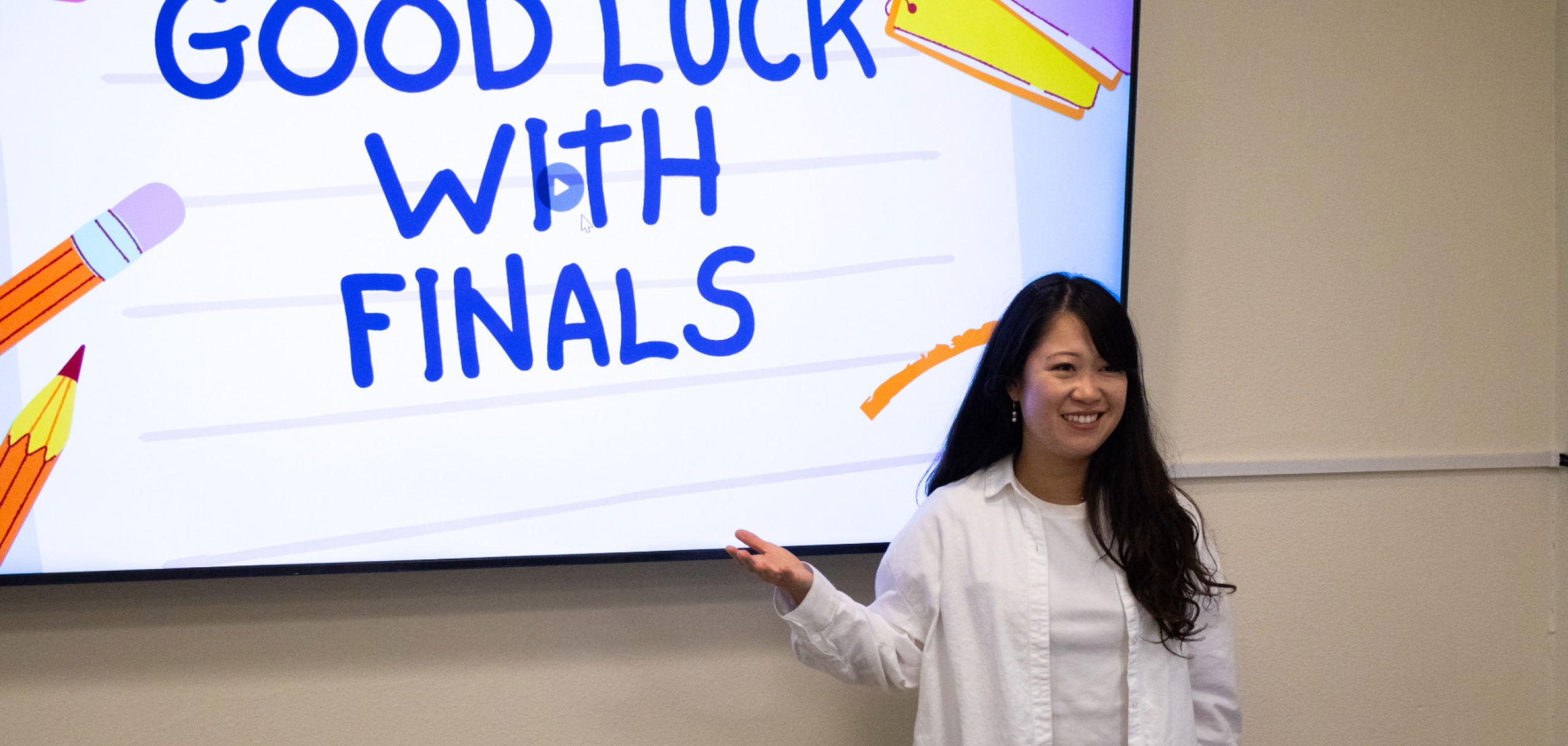 Leslie Ji is standing in front of a whiteboard with a "Good Luck with Finals" message written on it.