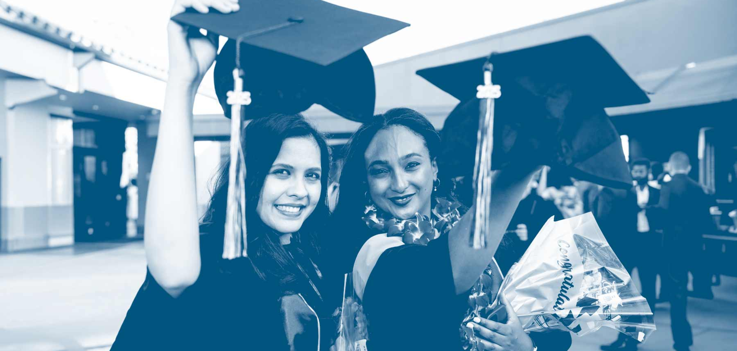 Two graduates in caps and gowns smile and raise their caps during a graduation celebration.