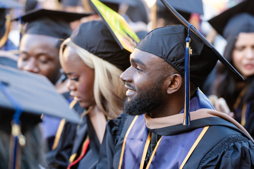 A SFBU graduate sits at commencement ceremony in their full regalia, in the midst of other SFBU graduates