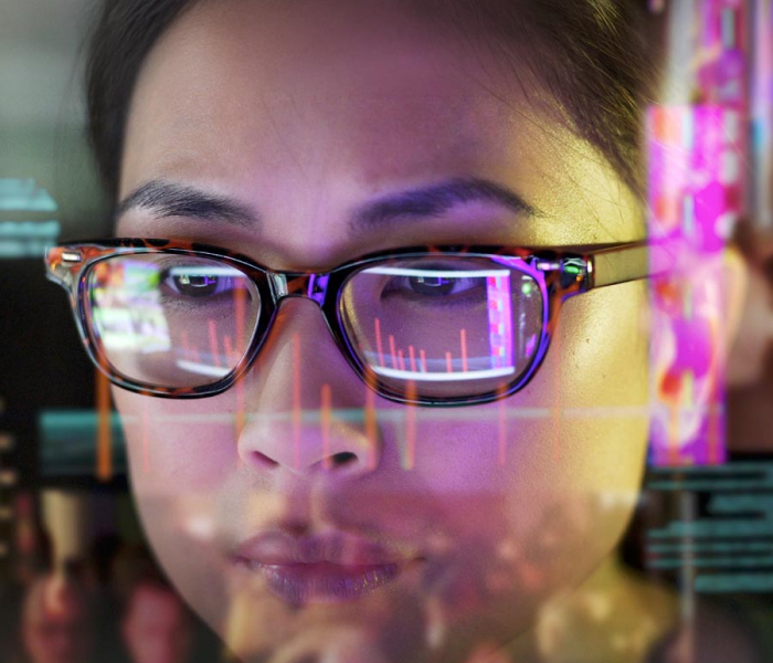 Close-up of a student wearing glasses analyzing data on a screen, with colorful charts reflected in the lenses.