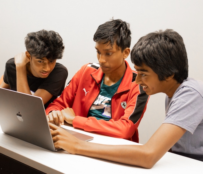 Three students are discussing by using the laptop in the classroom at the SFBU campus. 