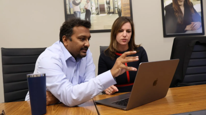 Two people reviewing information and discussing with a laptop in front of them.